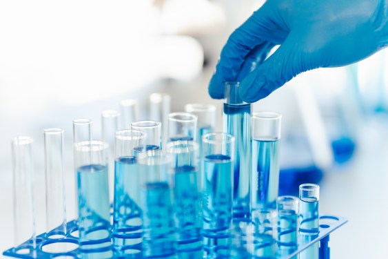specialty chemicals' testing in a lab; gloved hand picking up one of several vials of blue liquid
