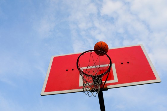 a basketball flies into the basket, against the blue sky, in an open area.